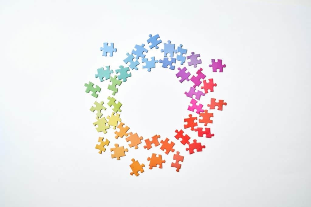 A circle formed by rainbow-colored puzzle pieces on a white background symbolizing unity and diversity.